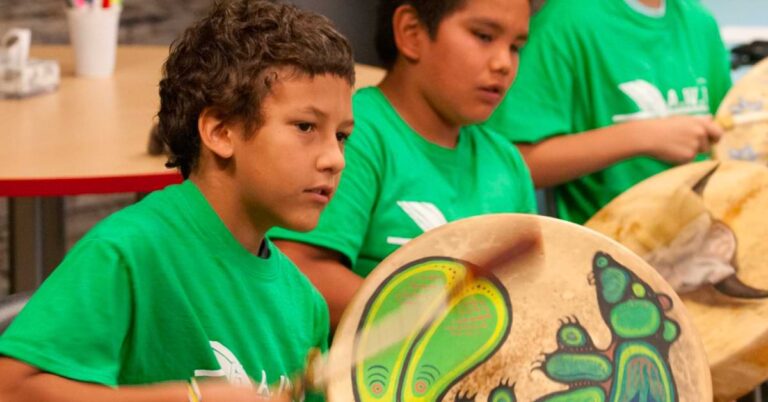 An indigenous male child wearing a green tshirt and playing a drum while in school
